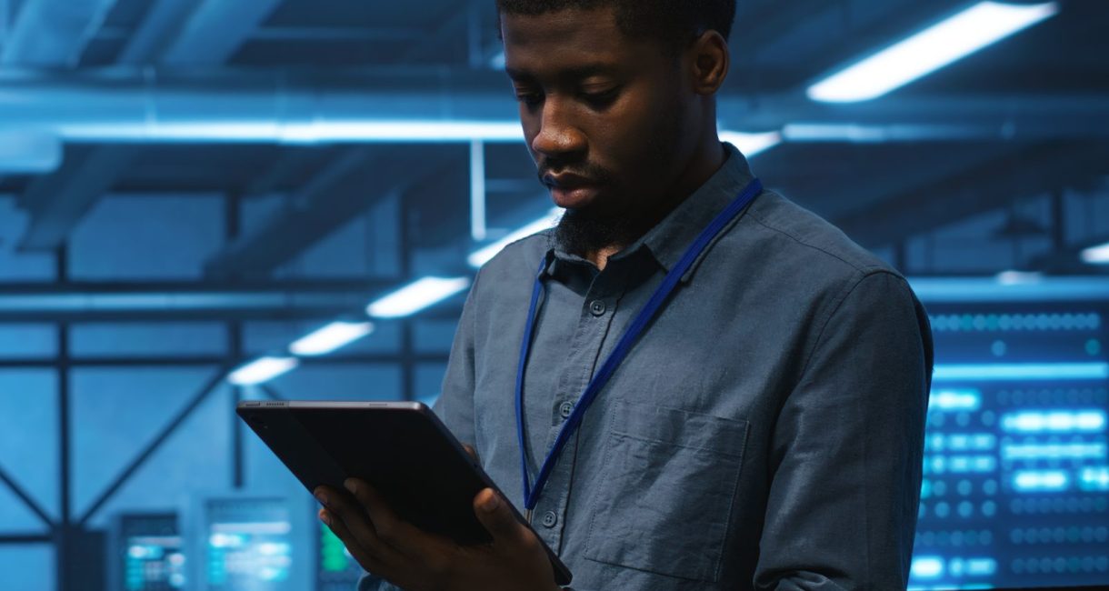 Technician in server hub using tablet to find hardware misconfigurations affecting rackmounts performance. Man checking data center infrastructure devices bottlenecks leading to errors